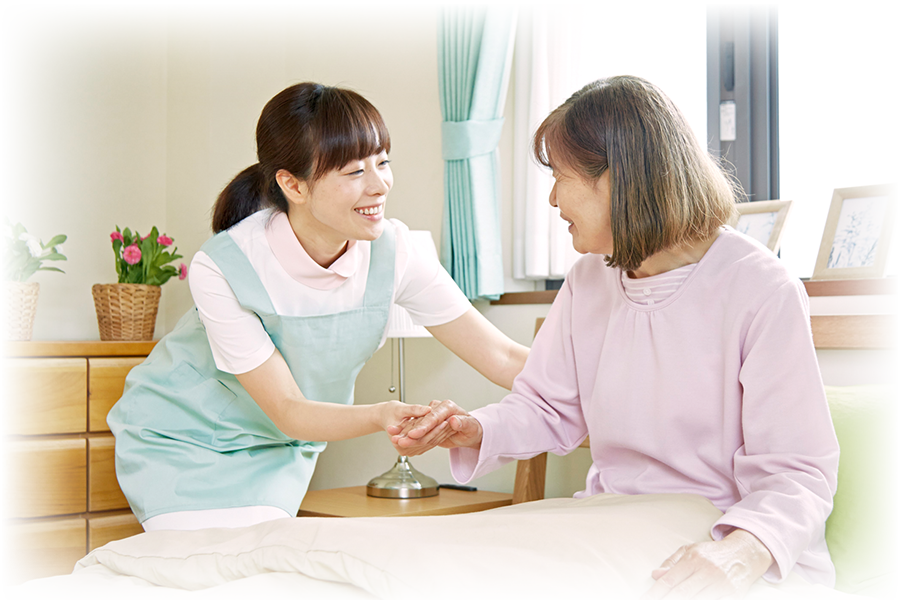 ベッドに座っている高齢者の手をとり手助けする職員